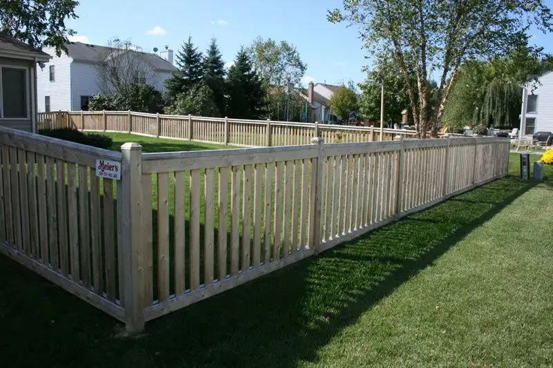 A wooden fence is surrounding a lush green yard.
