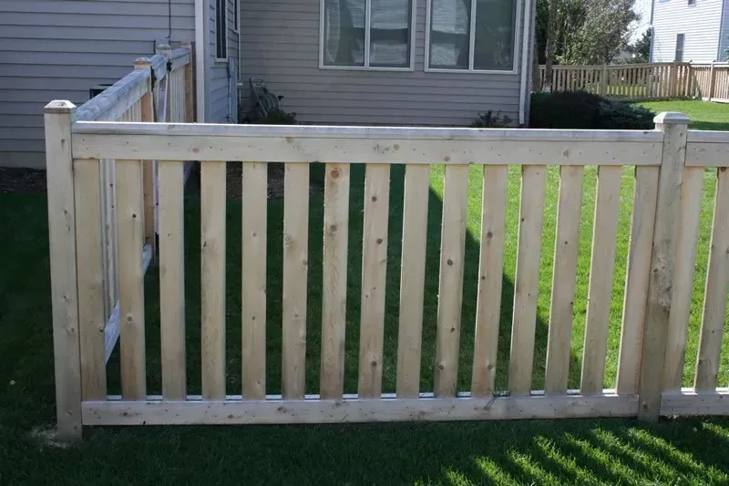 A wooden fence is sitting in the grass in front of a house.