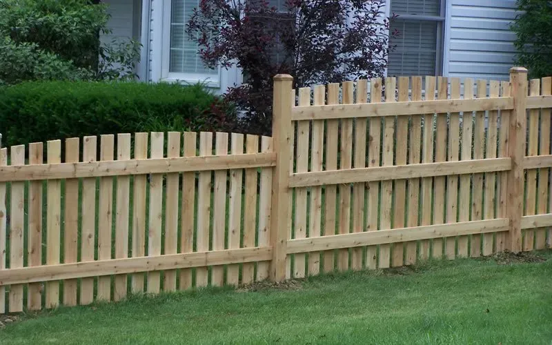 A wooden fence surrounds a lush green lawn in front of a house.