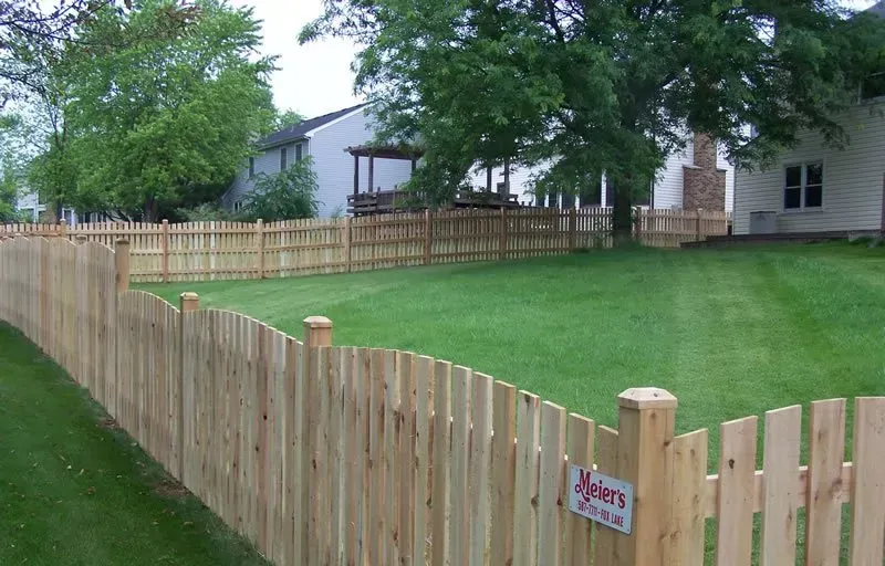 A wooden fence surrounds a lush green lawn in front of a house.