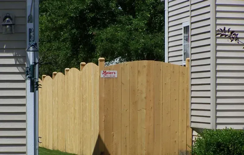 A wooden fence surrounds a house in a residential area.