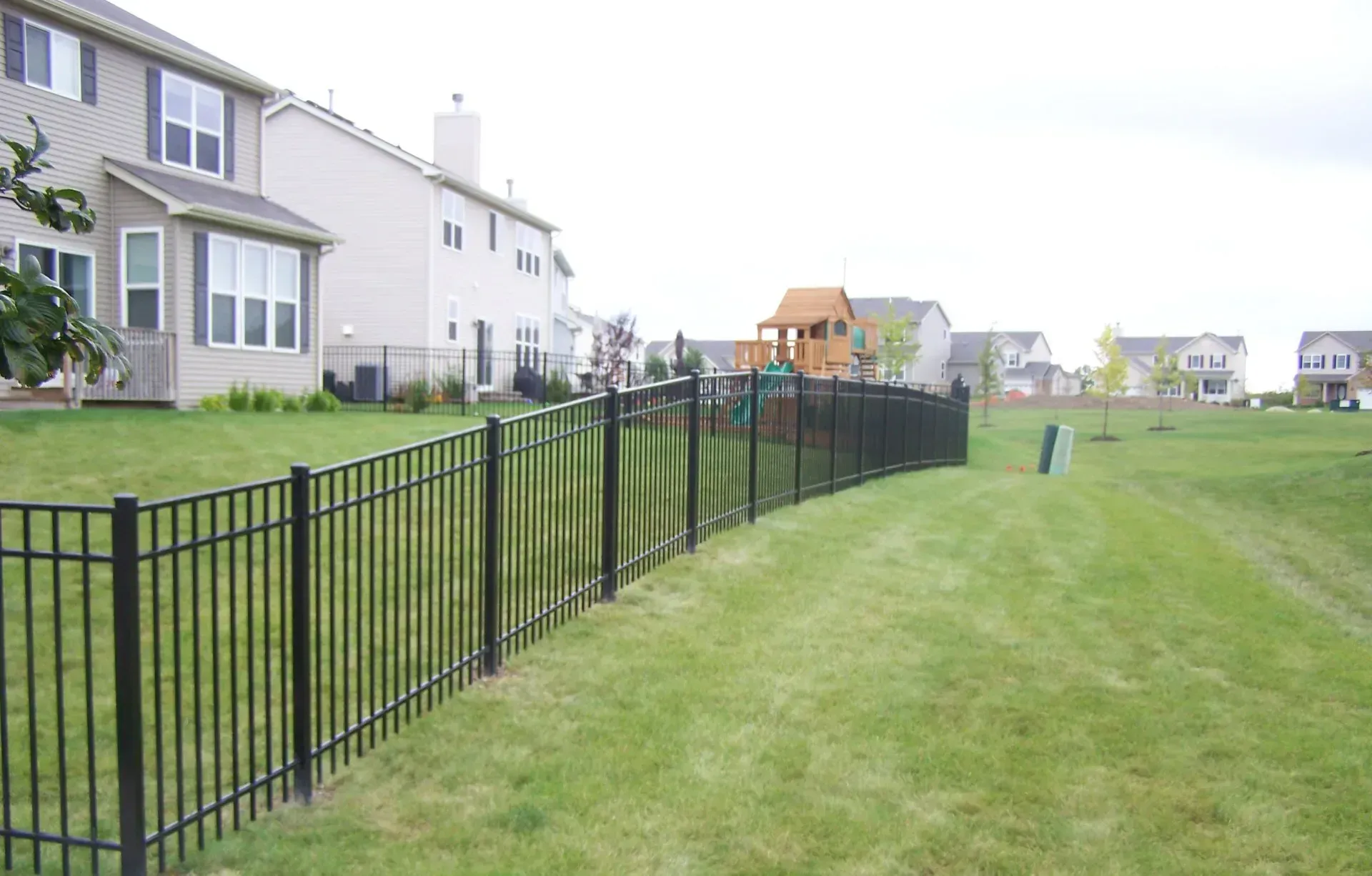 A black fence surrounds a lush green yard in front of a house.
