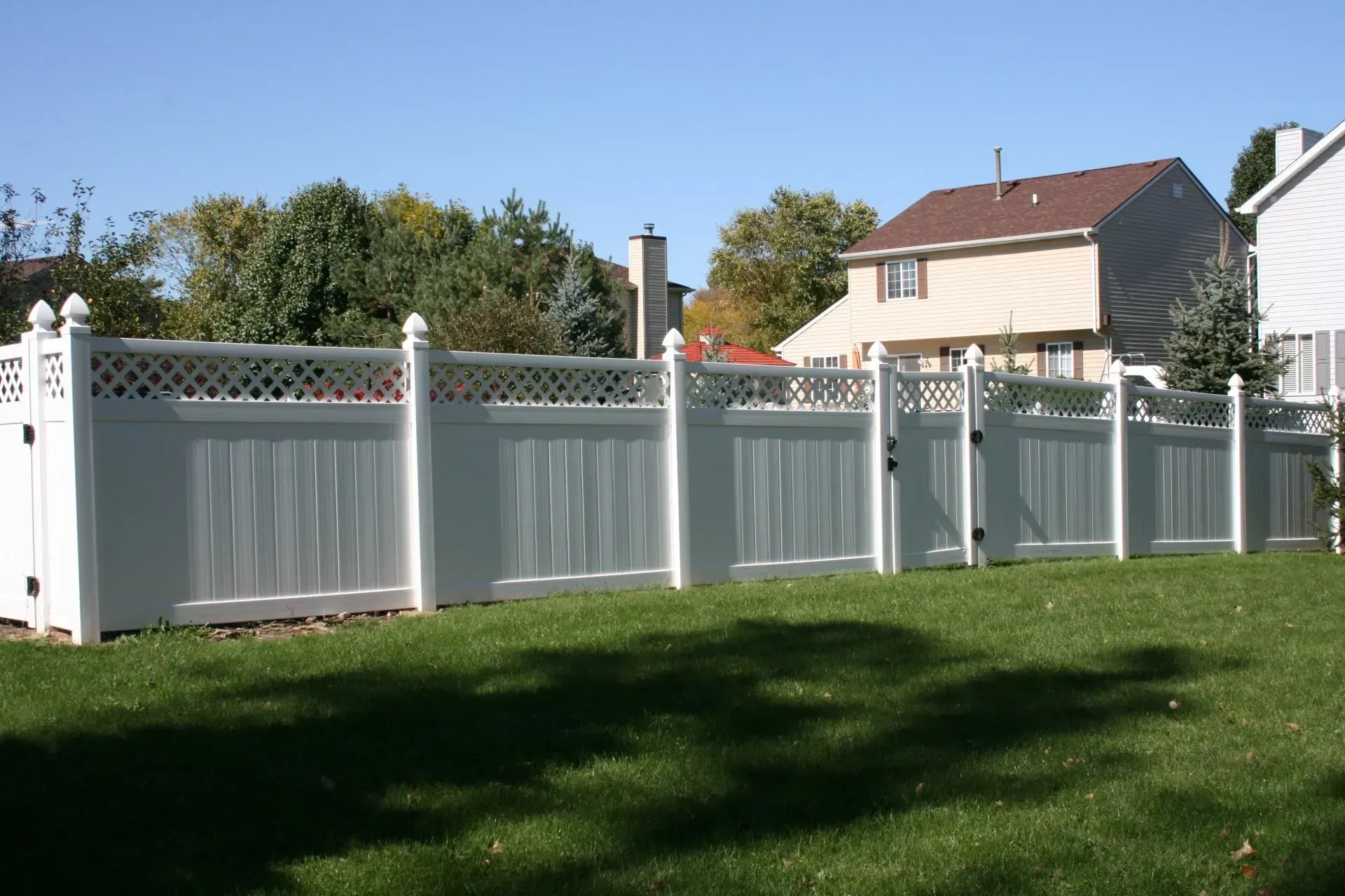 A white fence surrounds a lush green yard with a house in the background.