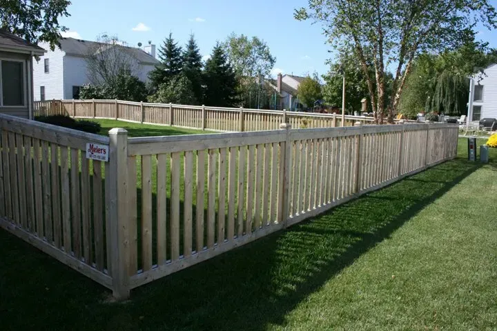 A wooden fence is in the middle of a lush green yard.