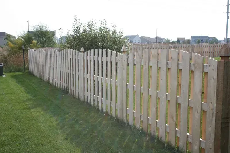 A long wooden fence surrounds a lush green yard.