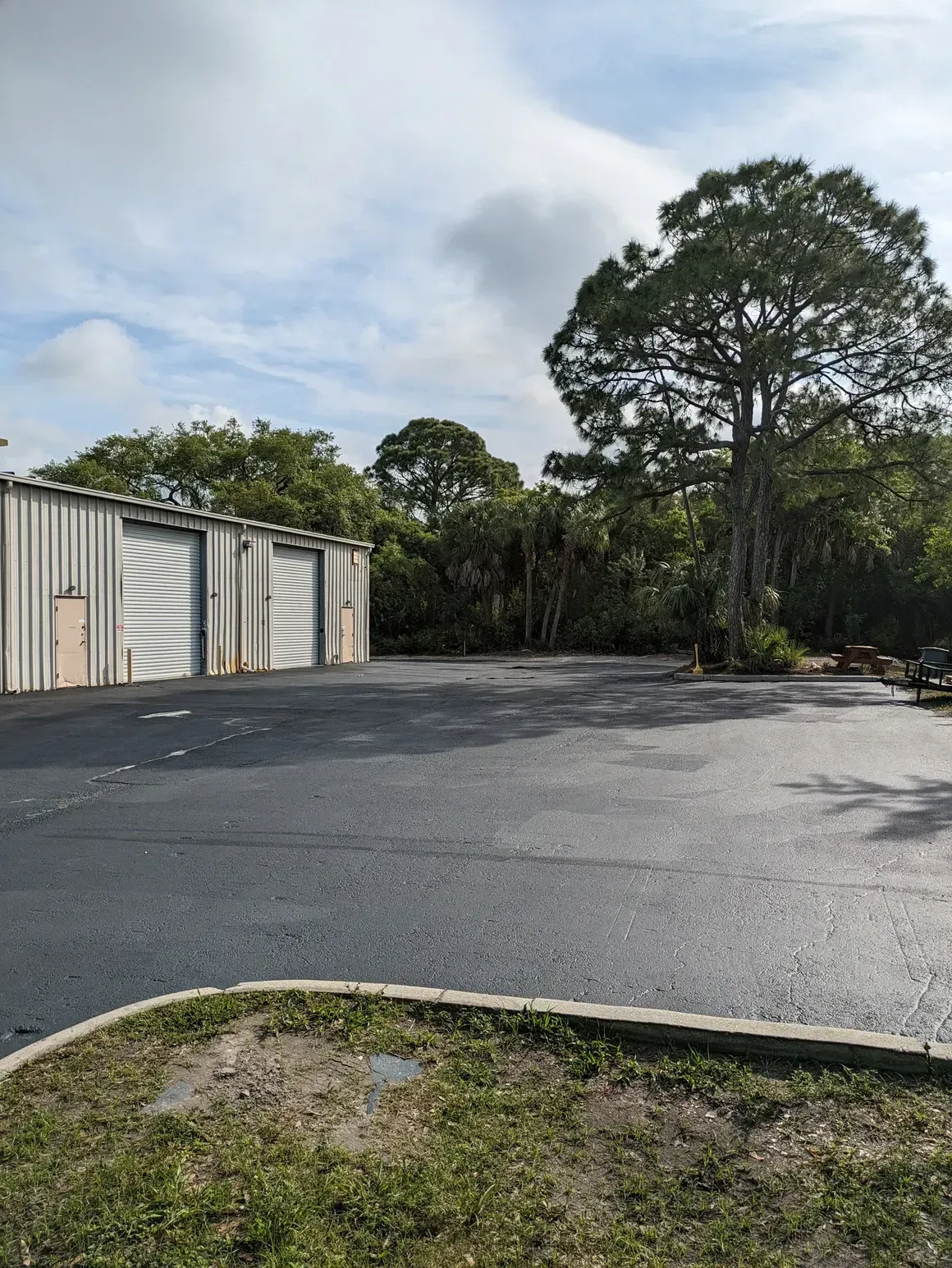 Empty paved lot beside metal storage units and trees under a cloudy sky