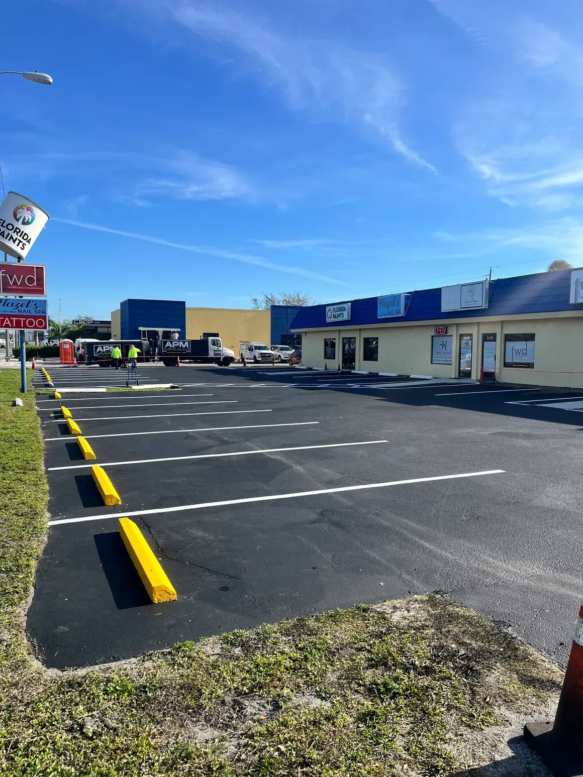 Empty parking lot beside a low strip mall under a bright blue sky.