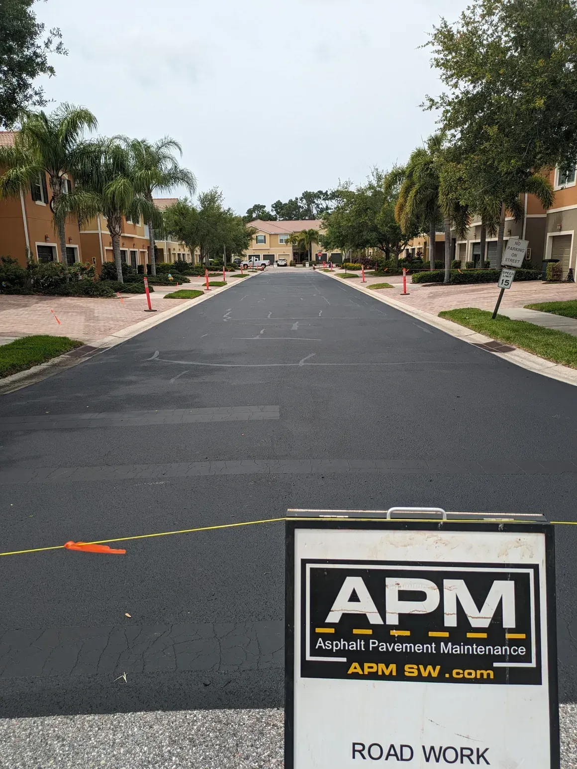 Residential street under paving work with an APM road-work sign in the foreground.