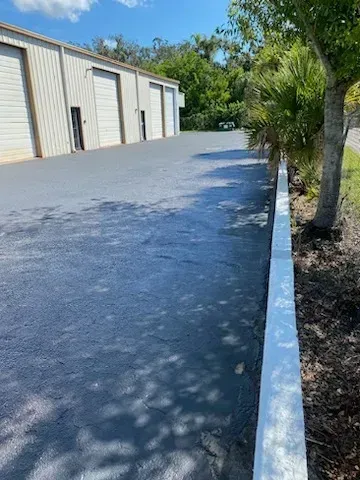 Industrial building driveway with white curb, trees, and blue sky on a sunny day
