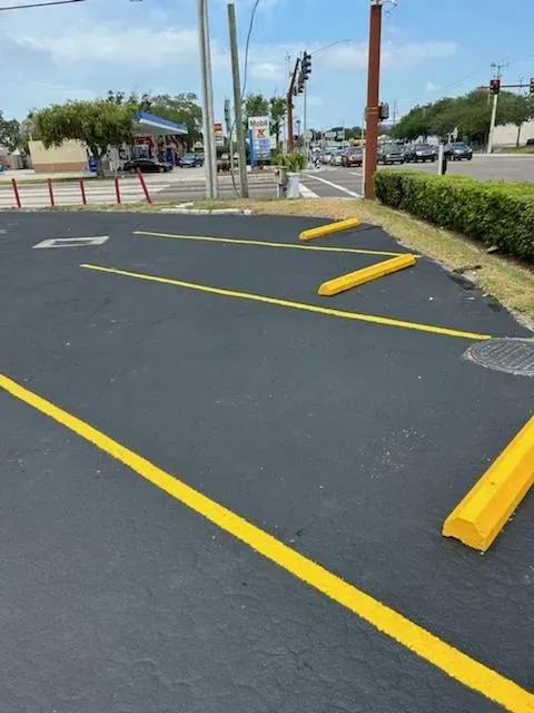 Empty parking lot with yellow barriers and painted lines near a road and landscaped area