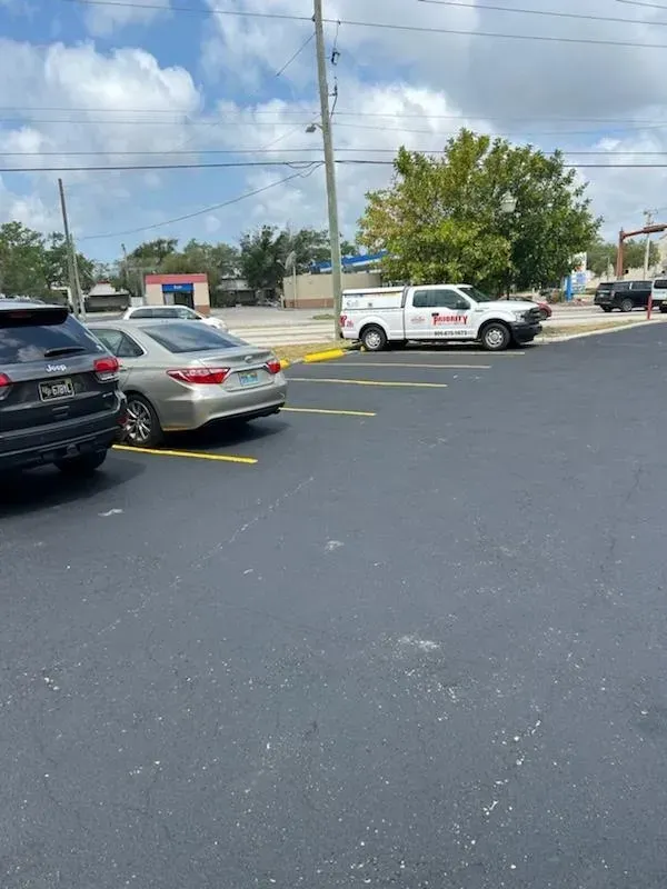 Parking lot with several parked cars, a white pickup truck, and trees under a partly cloudy sky