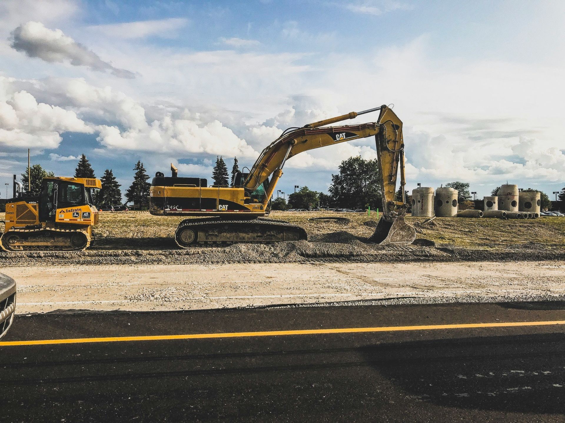 Yellow excavator at a construction site beside a road under cloudy skies