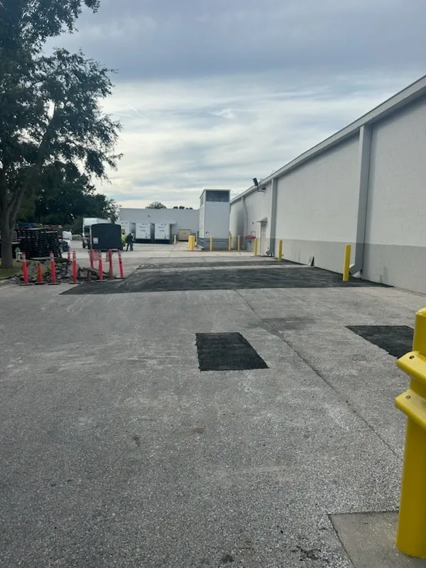 Industrial alley beside a white warehouse, with a yellow hydrant and red cones near parked equipment