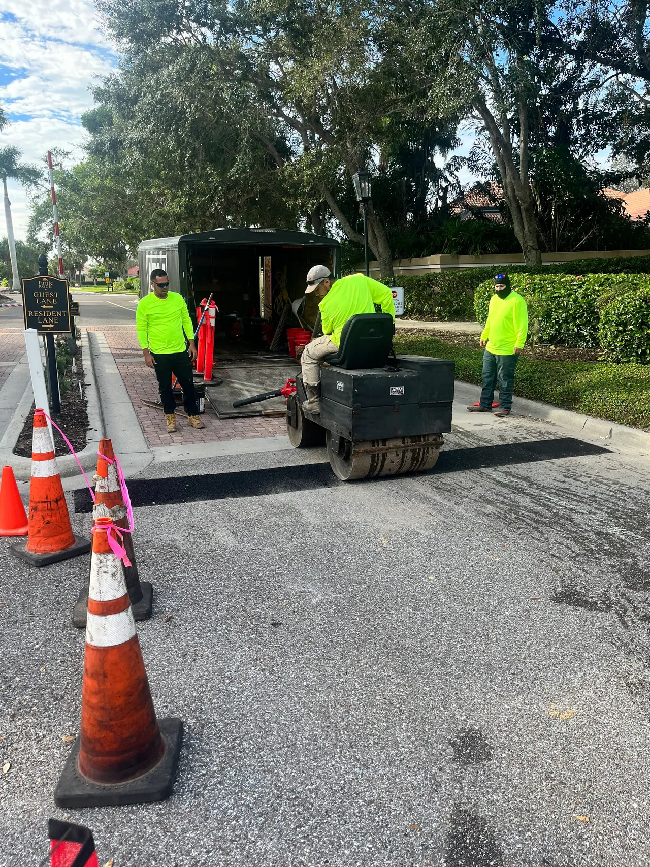 Workers in neon vests hauling a generator near orange traffic cones on a gravel roadside