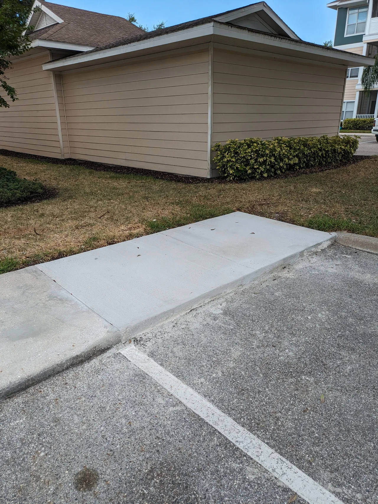Concrete accessible path beside a tan building and parking lot.