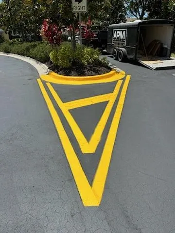 Yellow painted directional road marking around a landscaped island on a gray street.
