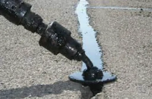 Black hose spraying water onto a cracked asphalt road, forming a small puddle.