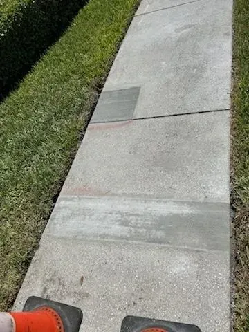 Sidewalk with concrete slabs beside a grassy lawn, viewed from a person standing near orange shoes.