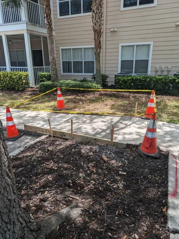 Apartment sidewalk under repair, blocked by orange cones and caution tape beside a building.