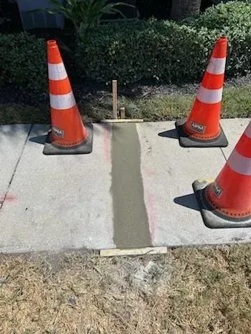Orange traffic cones blocking a narrow sidewalk ramp with a concrete repair strip in the center