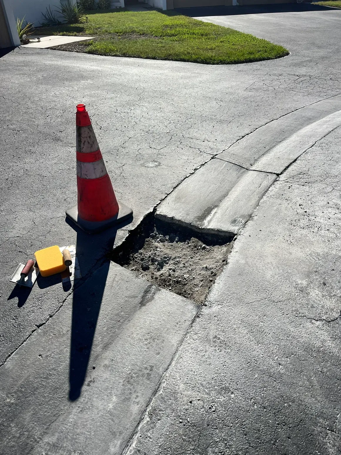 Orange traffic cone beside a pothole in a cracked curb lane