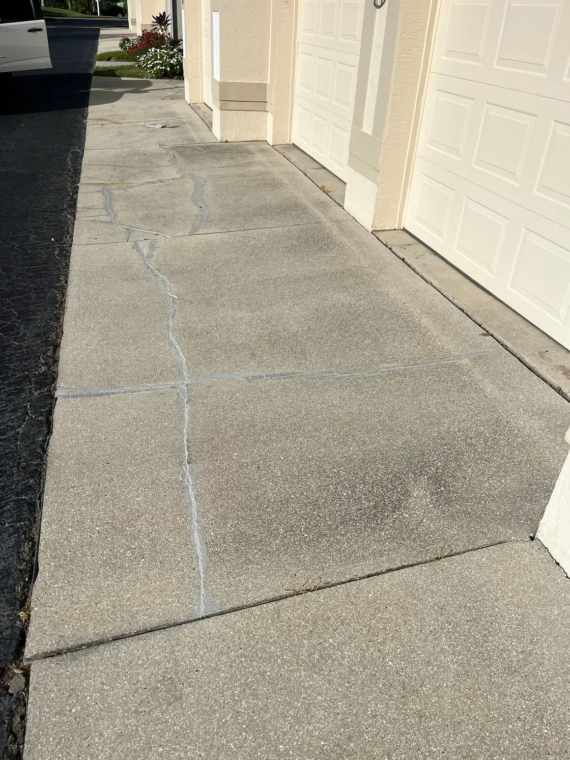 Concrete driveway beside beige garage doors, with a visible crack or repair seam.