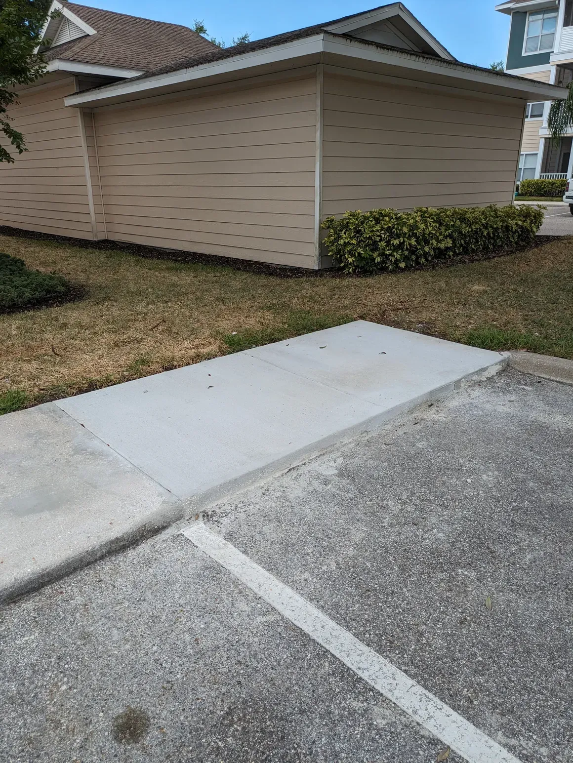 Concrete curb ramp at a parking lot beside a beige building and grassy area.