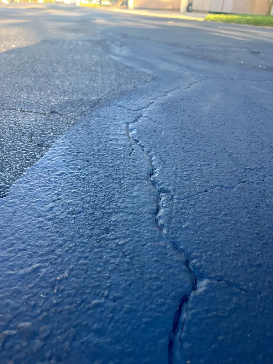 Cracked asphalt road surface with a long dark seam in sunlight
