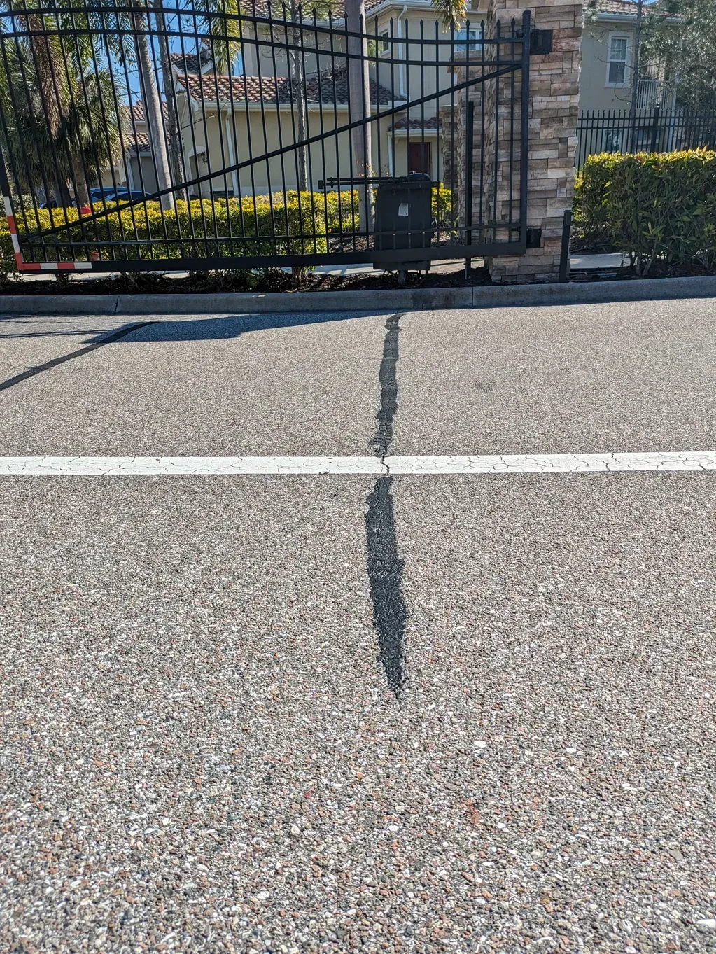 Cracked asphalt road leading to a black metal fence and a building in the background.
