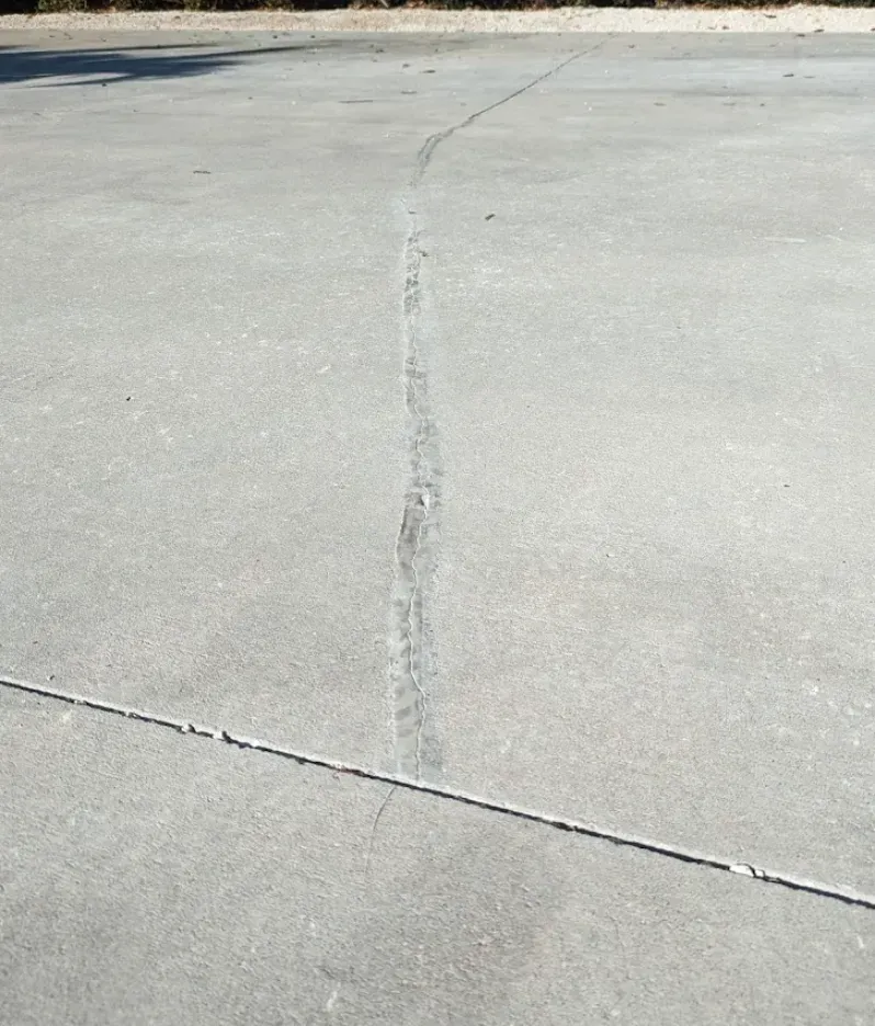 Cracked concrete pavement with a long vertical seam and a diagonal joint line.