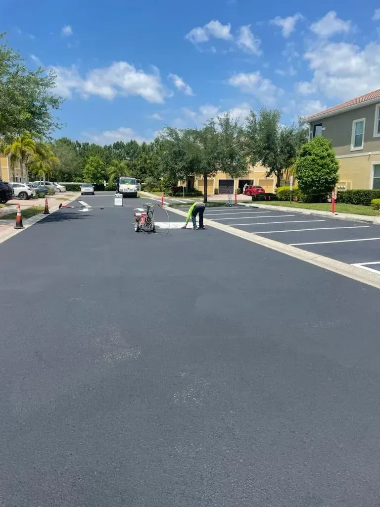 Roadwork on a suburban street with workers, cones, and fresh black asphalt under a clear blue sky