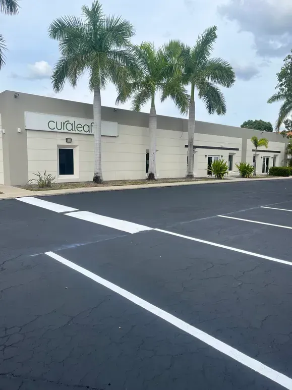 Curved office building with palm trees and empty parking lot under cloudy sky