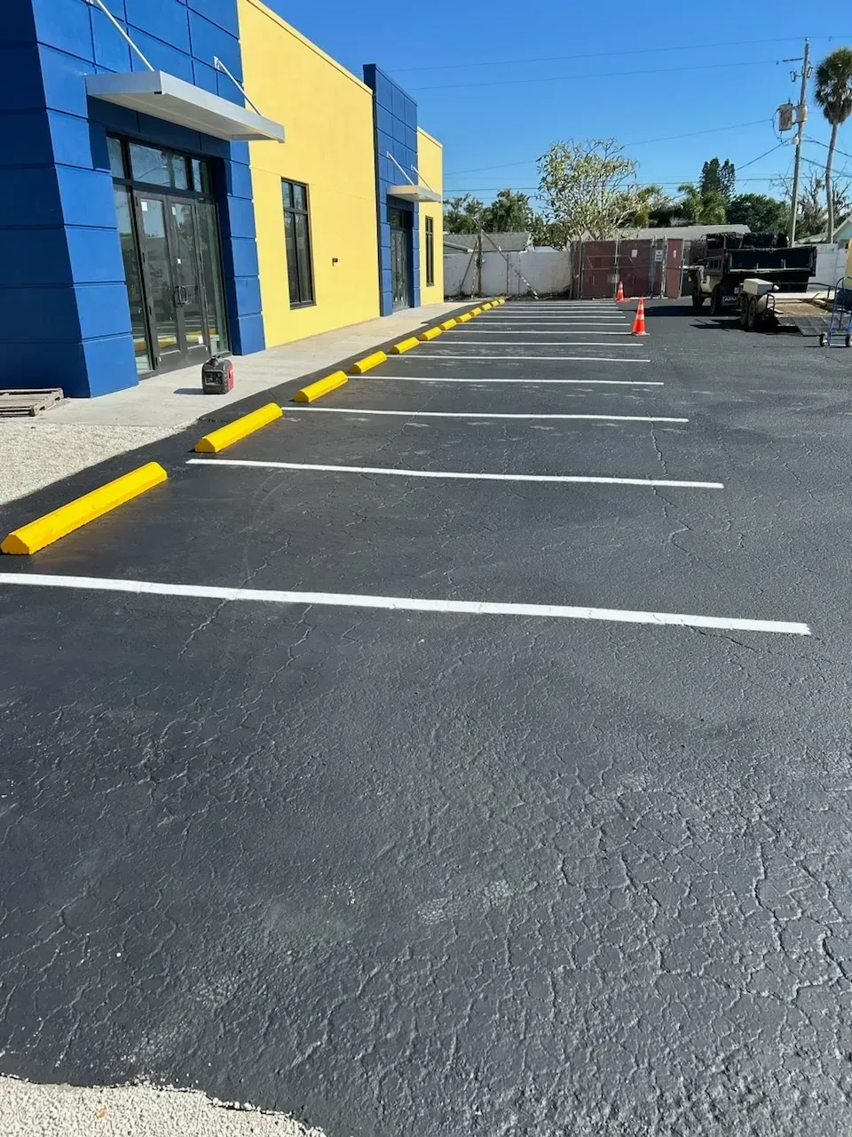 Empty parking lot beside a yellow-and-blue building with painted parking lines and cones