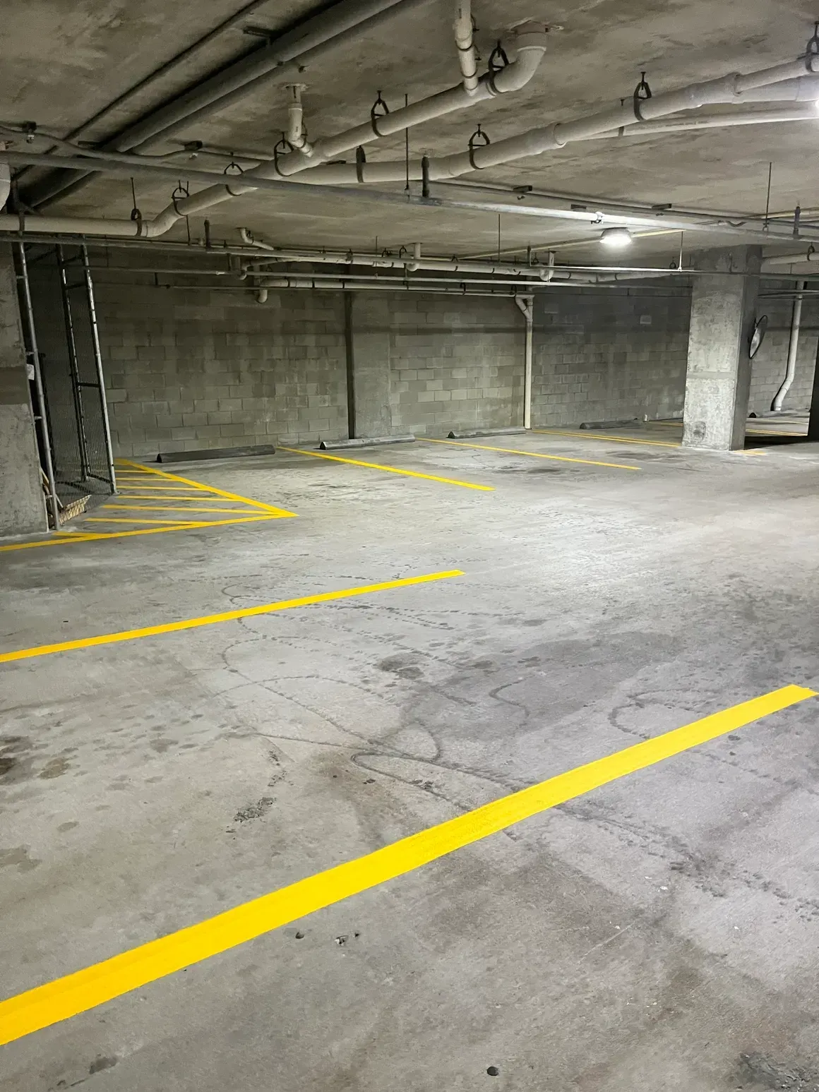 Empty concrete parking garage with yellow painted parking lines and ceiling pipes