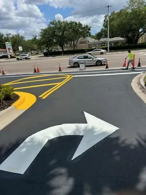 Road construction with painted lane arrows, cones, and a worker directing traffic near a parked car