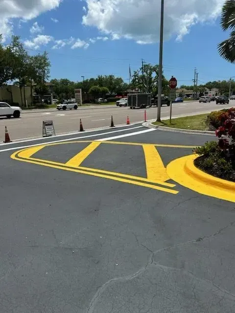 Parking lot entrance with yellow-striped curb ramp, traffic cones, and a stop sign on a sunny day
