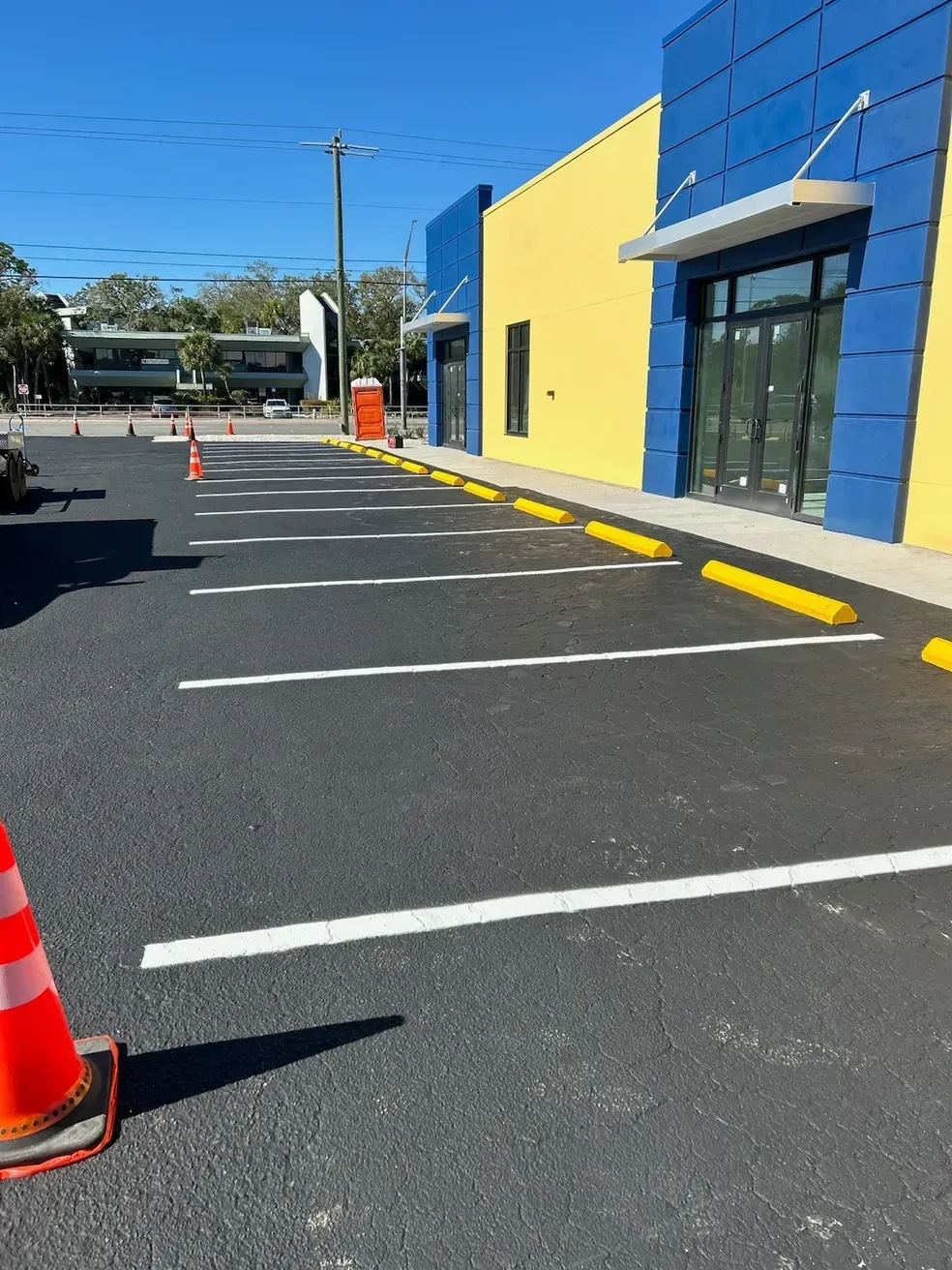 Empty parking lot beside a blue-and-yellow building with orange cones and painted parking lines