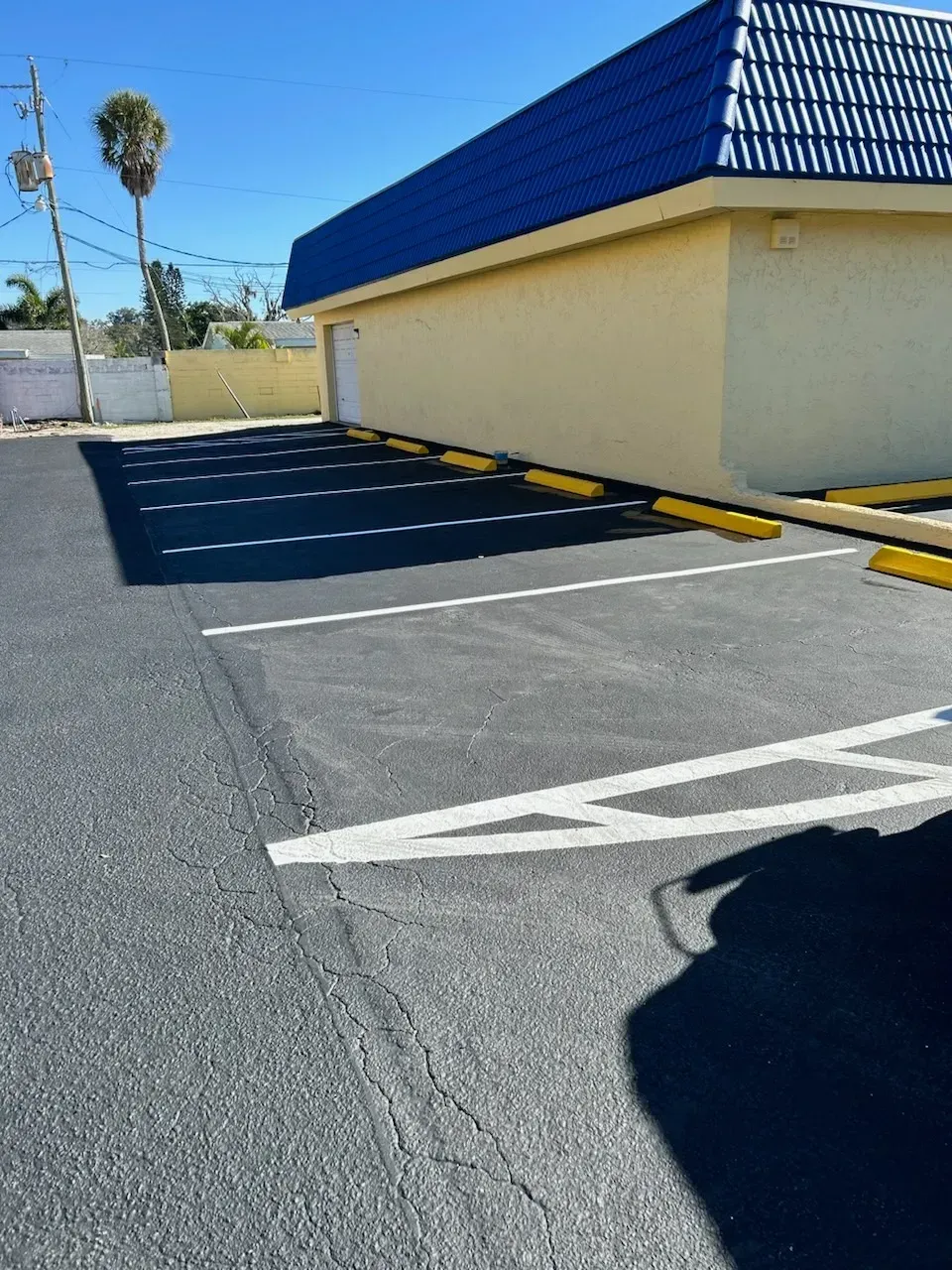 Empty parking lot beside a beige building with a blue roof and white directional arrow markings.