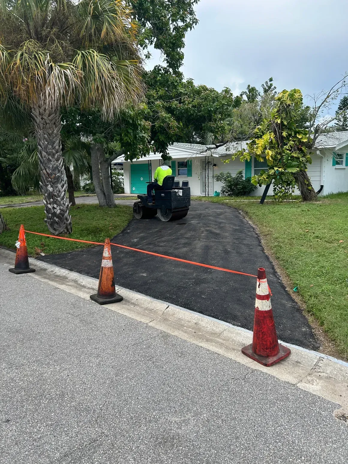 Worker on a black asphalt path beside a white building, with orange cones marking the area.
