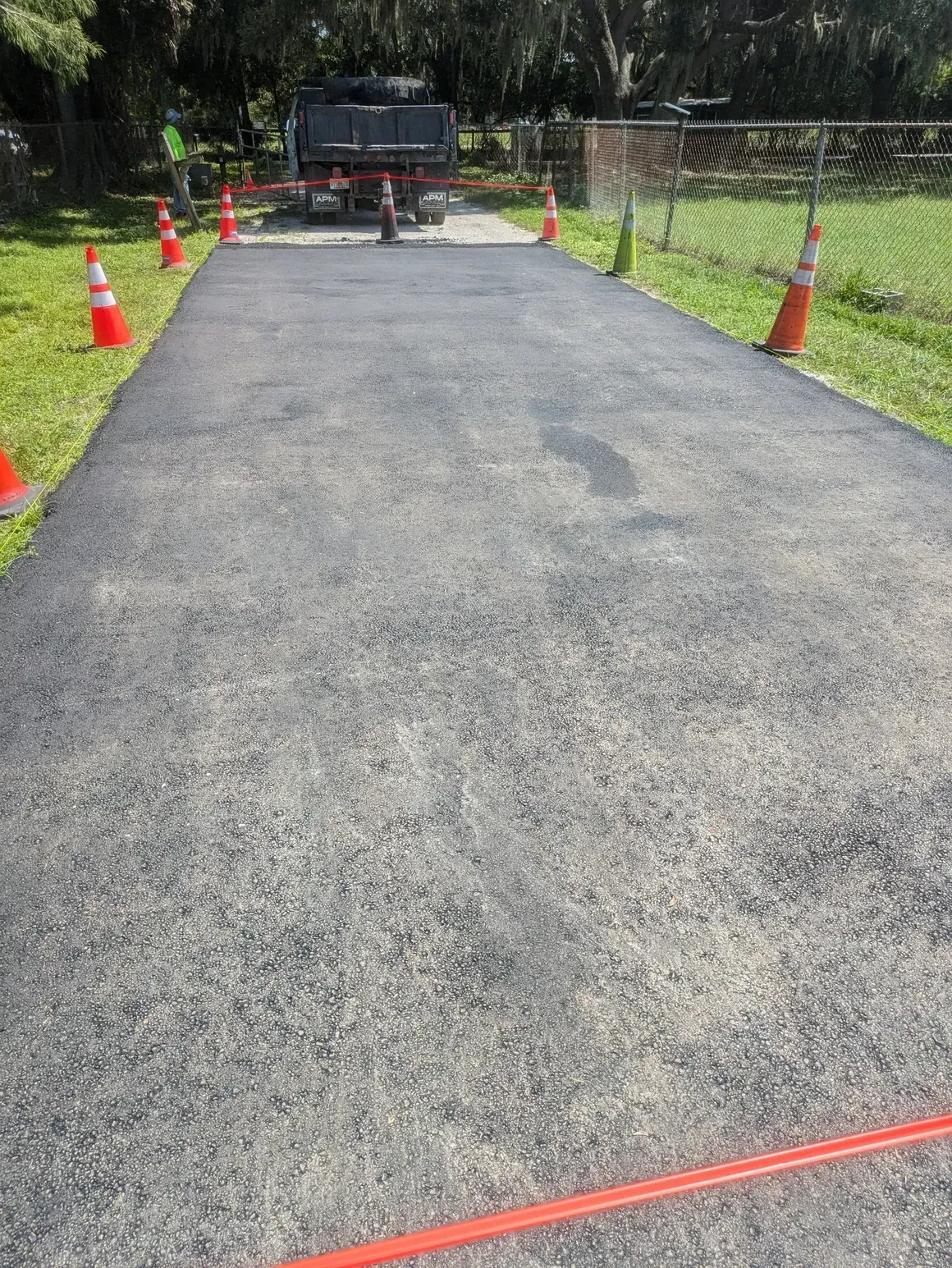 Freshly paved driveway with orange cones and a truck at the far end