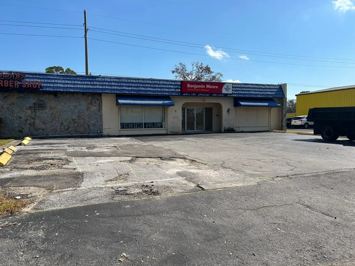 Small roadside storefront with blue awning and parking lot, a yellow truck parked on the right.