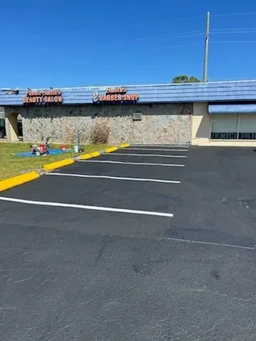 Empty parking lot beside a low stone building with blue roof and yellow curb under a clear sky