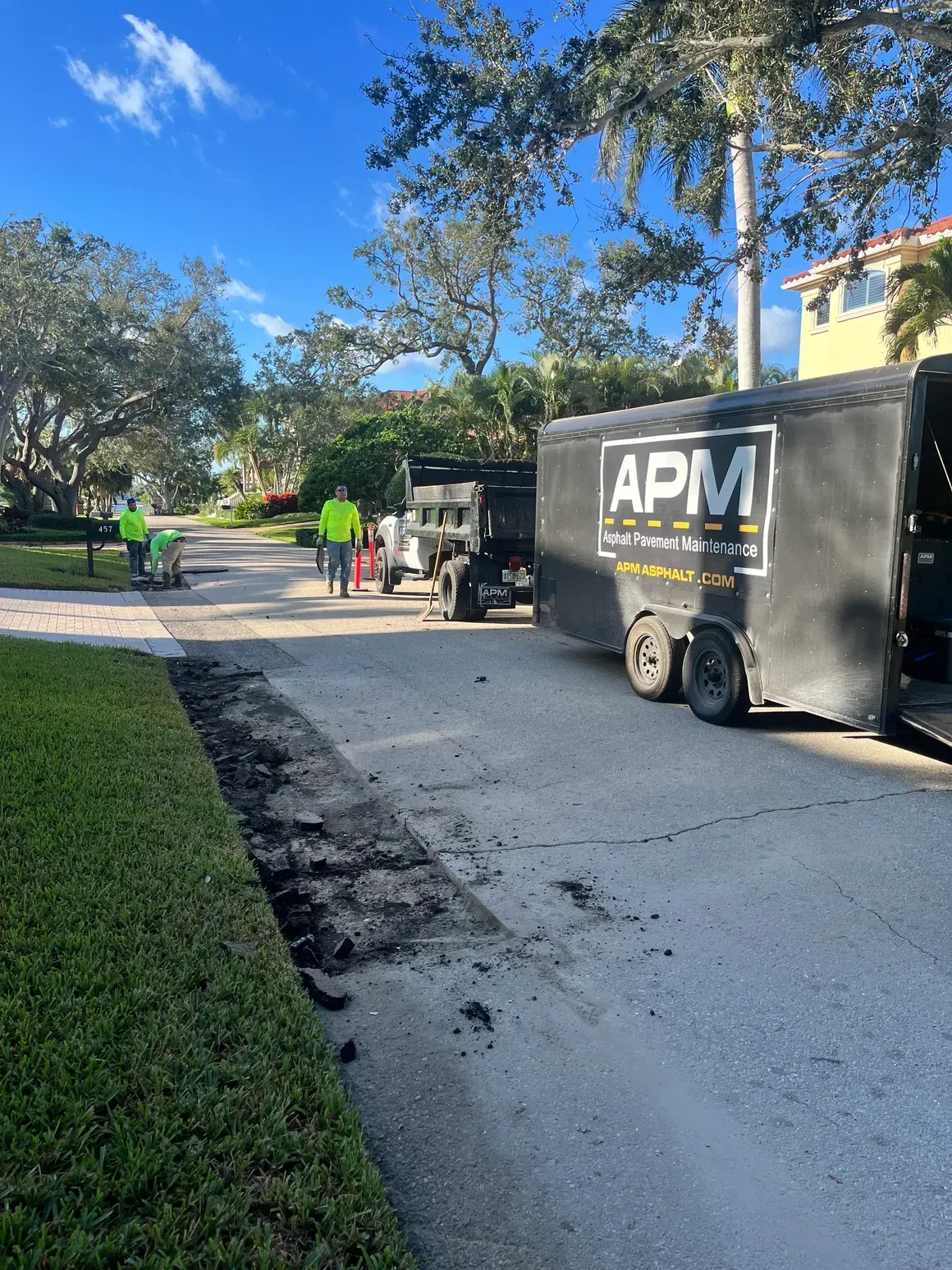 Workers with APM trailer paving a driveway beside a house on a sunny day