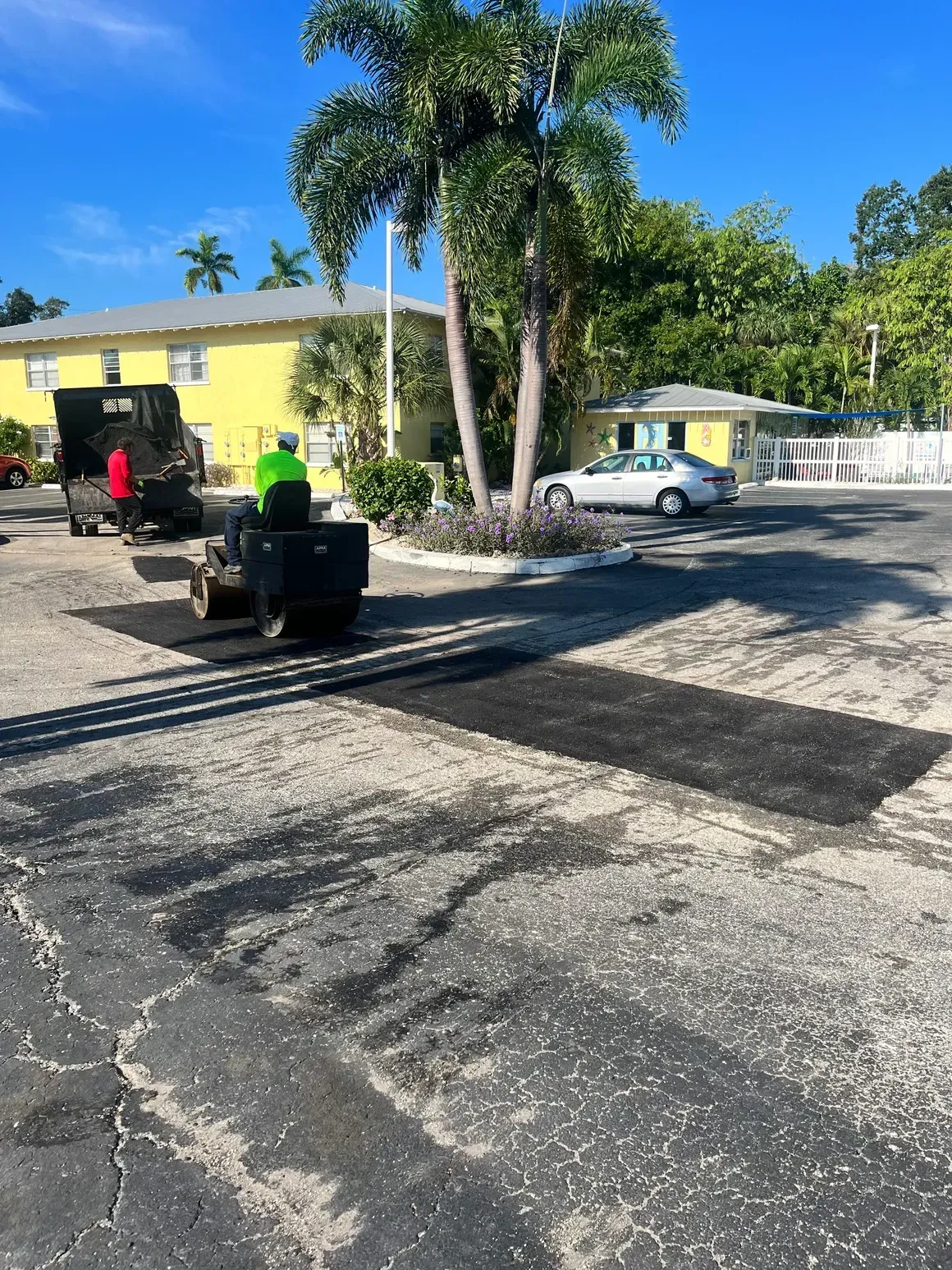 Two lawn mowers on a sunlit paved lot beside a yellow building and palm trees