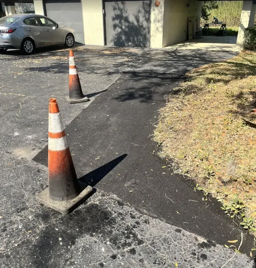 Two orange traffic cones marking a cracked driveway beside a parked silver car and a house garage
