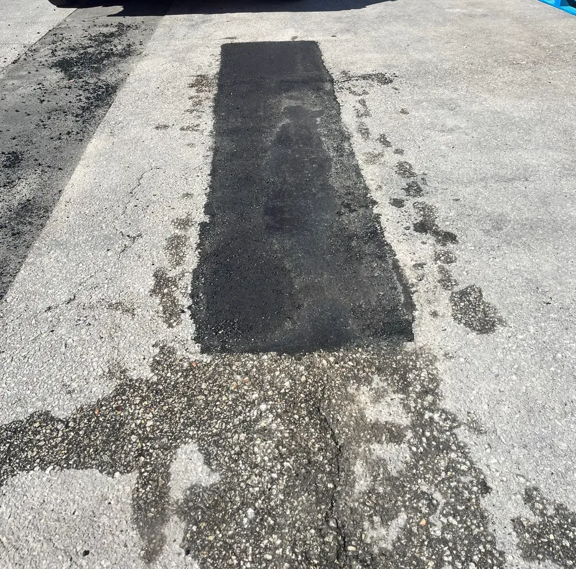 A patched section of rough asphalt road with a dark rectangular repair in the center.