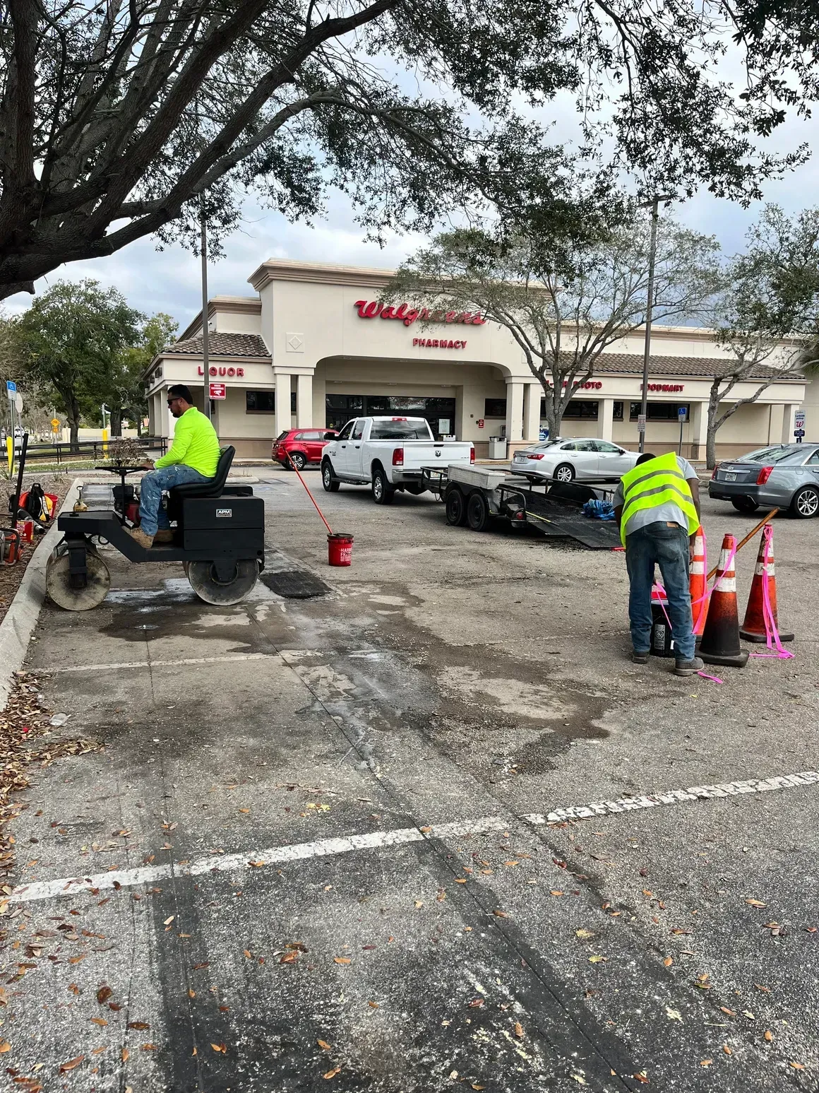 Workers in neon vests repairing a parking lot outside a Walgreens under overcast trees
