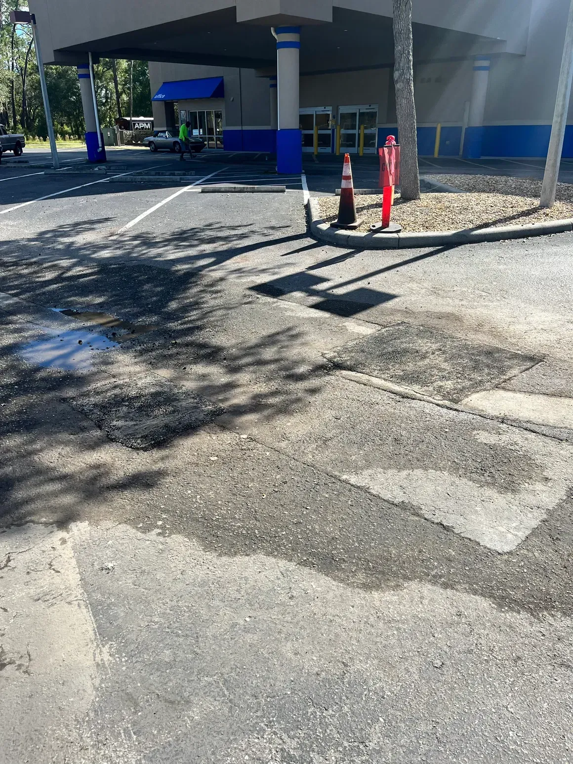 Cracked asphalt driveway beside a building entrance with three orange cones and blue columns.