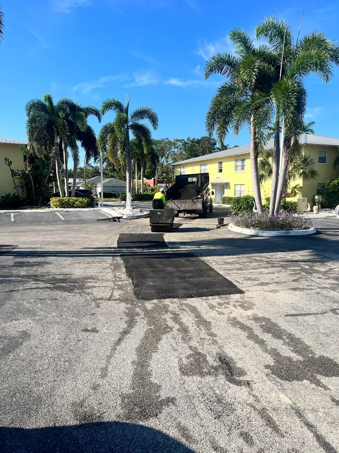 Parking lot with a black utility truck, palm trees, and yellow buildings under a bright blue sky