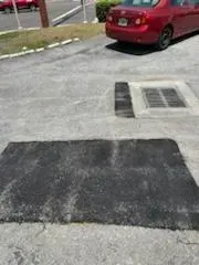 Parking lot with black speed bump, storm drain, and a red car parked nearby